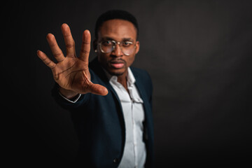Young man in African American suit standing in front of camera with hand in front as stop sign, on...