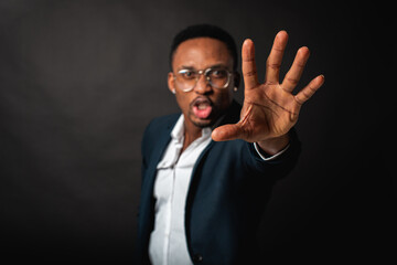 Young man in African American suit standing in front of camera with hand in front as stop sign, on dark background. Selective focus. Sign language.