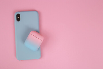 Phone in a silicon case and a case for headphones on a pink background with copy space. Stylish...