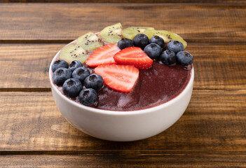 Brazilian typical acai bowl with kiwi, blueberry and strawberry over wooden table