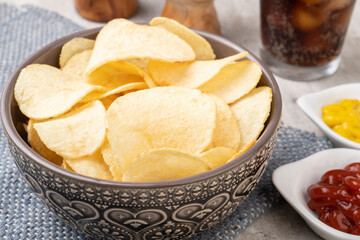 Potato chips in a bowl, pepper, salt, mustard, ketchup and a glass of soda