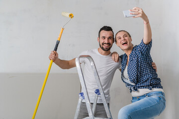 Man and woman taking selfie on the background of the wall with a stepladder and roller. Medium shot