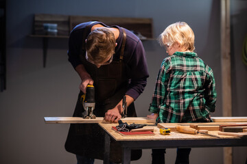 an experienced carpenter and his young apprentice make wood crafts in their workshop