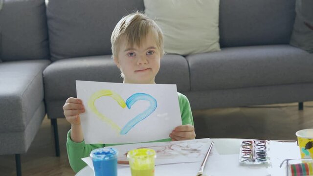 Boy with Down Syndrome holding a picture with yellow and blue heart
