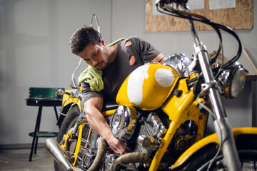Fototapeta na wymiar A handsome young male biker in his garage is preparing his motorcycle for the season. Repair and tuning