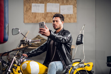 Fototapeta na wymiar A stylish guy on a yellow cool motorcycle takes a selfie in a garage or car repair shop.