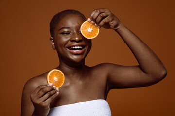 Cheerful Black Lady In Towel Posing With Orange Fruit Slices Near Face