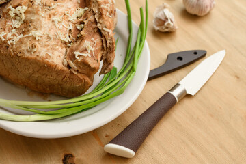 baked meat on a plate, green onion and garlic on wooden background, home cooking