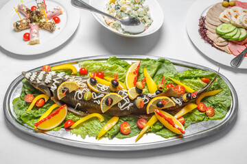 Cooked sterlet lies on a platter , decorated with lettuce leaves, tomatoes, oranges, olives.