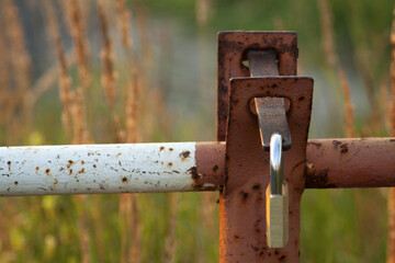 An old and rusty entry barrier, locked with a padlock. The faded and flaking paint contrasts with the green of the tall grass surrounding it.
