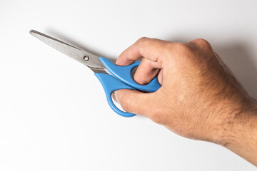 Hand holding blue metal scissors laying over a white background