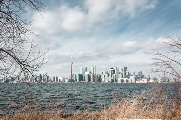 Cityscape of Toronto skyscrapers, with vegetation in the foreground and a lake. Blue cloudy sky 