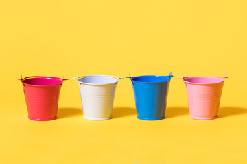 Four multi-colored toy buckets on a yellow background. White blue pink and red bucket standing in a...