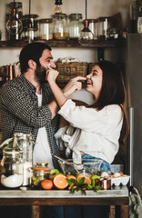 Young happy couple having fun during cooking together in kitchen. Positive caucasian man and brunette woman putting flour on each other faces, flirting, laughing, baking citrus cake. Valentines Day
