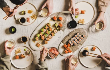 Foto op Plexiglas Quarantine Japanese sushi dinner from delivery or takeaway service at home. Flat-lay of people eating salmon, crab, prawn rolls variety, wasabi, ginger over light tablecloth background, top view © sonyakamoz