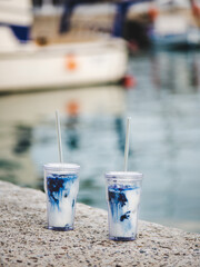 Blue iced matcha latte drink in reusable eco-friendly glasses with glass straws at sea coast in Mediterranean town outdoors, selective focus. Take away food during lockdown concept