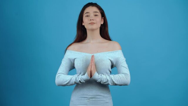 The young woman puts her hands together to pray, at the end she smiles. Asian with dark hair, dressed in a blue blouse, isolated on a dark blue background in the studio. Lifestyle concept. Portraits