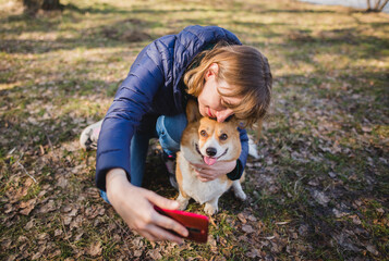 a  young woman doing a selfie with a welsh corgi pembroke dog during a walk in a park