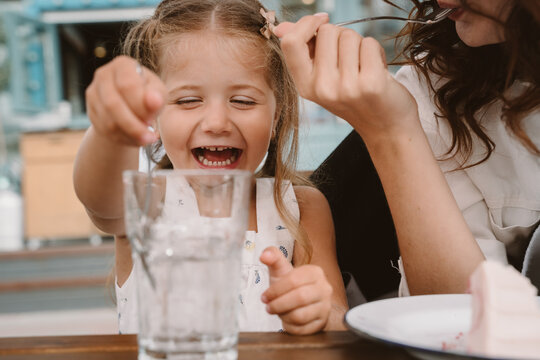 Little girl with mom playing with ice cubes in a cozy cafe.