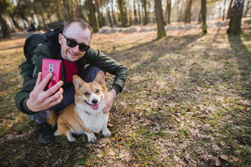 Naklejka na ściany i meble a young man doing a selfie with a welsh corgi pembroke dog during a walk in a park