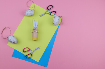 scissors and paper.
Colored paper with scissors and Easter eggs with bunny on the left on a pink background with place for text on the right, top view close-up.