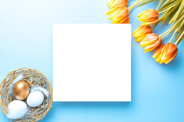 Naklejka na ściany i meble Easter flat. Golden, white colour egg in basket with spring tulips, feathers on pastel blue background in Happy Easter decoration. Spring holiday top view concept.