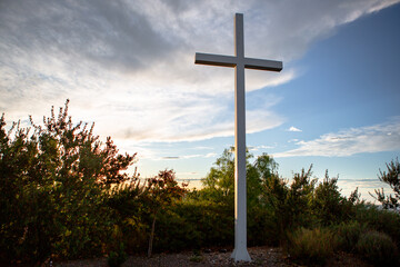 Sunlight bursts behind a mountain top cross of Jesus during golden hour at sunrise on Easter...