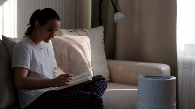 Modern air humidifier, aroma oil diffuser at home. Improving the comfort of living in a house, Improving the well-being. Ultrasonic steam technology. Woman reading book on background