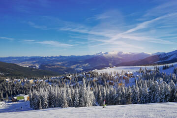 Snowy mountains and ski lifts. Skiers and snowboarders skiing downhill to village.