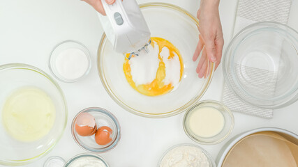 Woman hands mixing egg yolks with sugar in a glass bowl using an electric mixer. Close up baking process