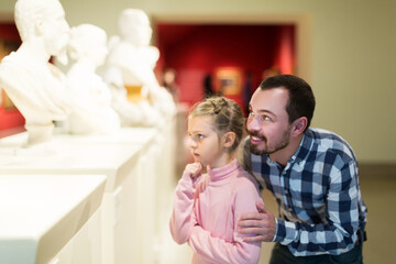 Obraz na płótnie Canvas Positive young father and daughter looking at classical statues in museum