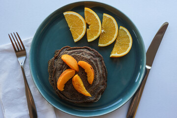 Plate of buckwheat pancakes with peach and orange slices in playful table setting.