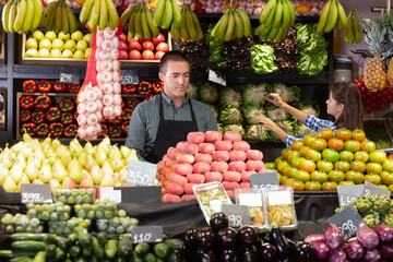 Man and woman shop assistants laying out fruits and vegetables behind the counter in store