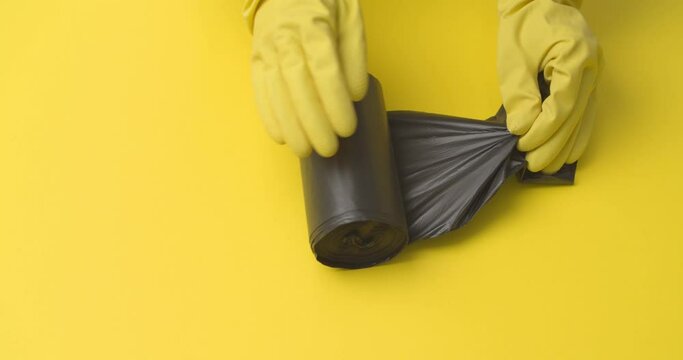 Hands in rubber gloves taking one garbage bag from roll on color background