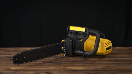 Black and yellow electric saw on a wooden table on a black background.