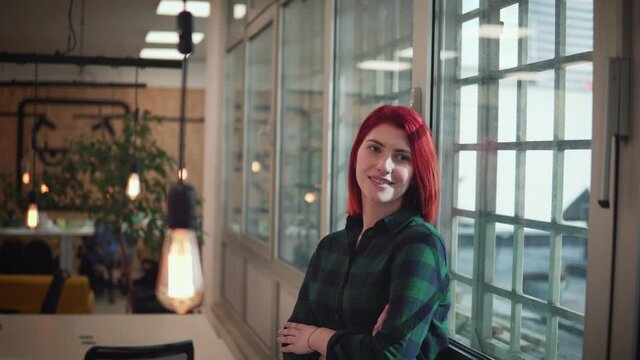 Red hair smiling businesswoman is standing in her office