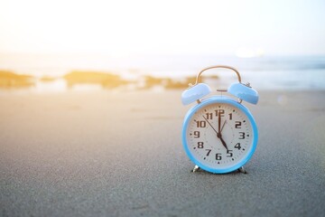 Blue vintage alarm clock on the beach in evening time with sunlight. Summer travel concept. Vacation and holiday concept. Get off work concept.