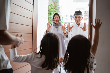 excited asian muslim grandparents visiting their grandchildren at home