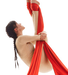 Young girl exercises on red aerial silks in studio