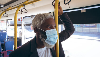 African american senior man wearing face mask standing on bus looking out of window