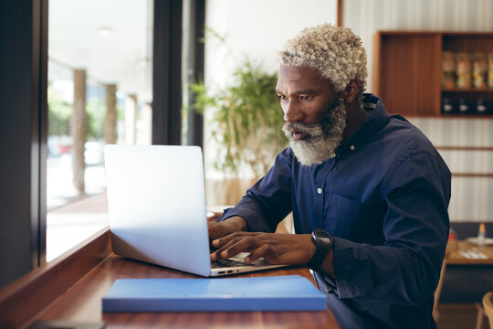 African american senior man sitting at table in cafe working using laptop