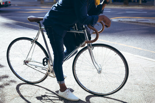 Low section of african american senior man leaning on bicycle in street talking on smartphone