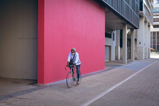 African american senior man riding bicycle in the street past red wall