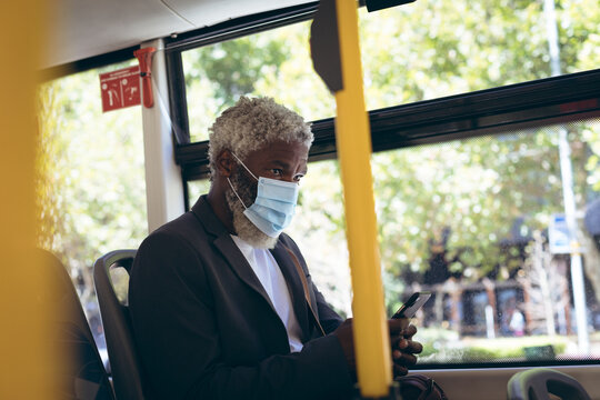 African american senior man wearing face mask sitting on bus using smartphone