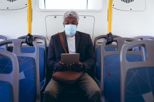 African american senior man wearing face mask sitting on bus using digital tablet