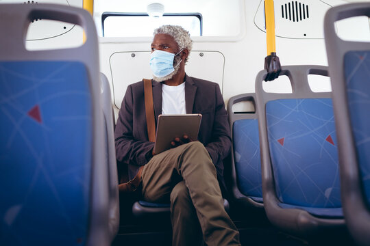 African american senior man wearing face mask sitting on bus using digital tablet