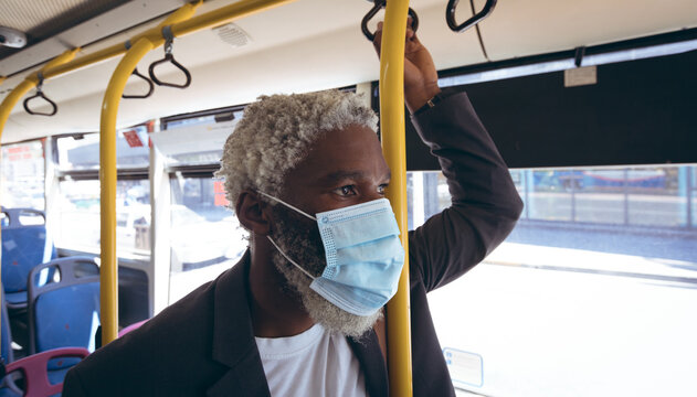 African american senior man wearing face mask standing on bus looking out of window