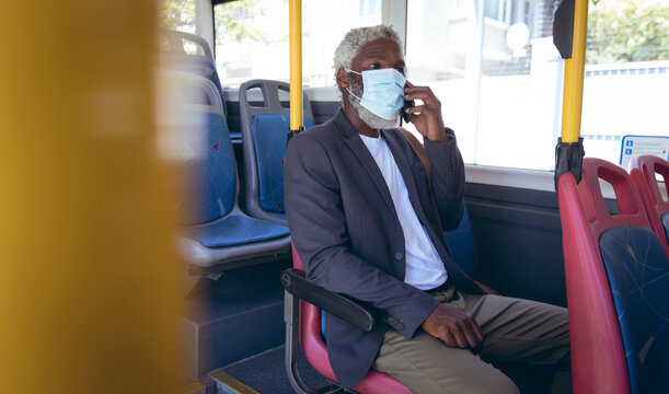 African American Senior Man Wearing Face Mask Sitting On Bus Talking On Smartphone