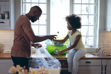African american girl and her father sorting recycling together in kitchen