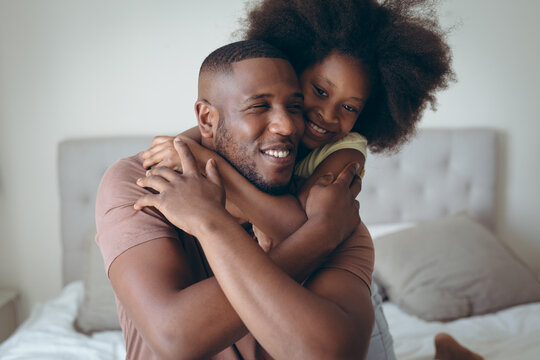 African american man and his daughter embracing on bed
